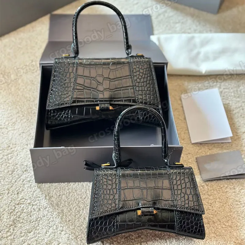 Two black crocodile-embossed top-handle handbags displayed with an open box, tissue paper, and cards on a carpet.