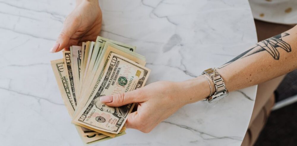 Hands holding U.S. dollar bills over a marble table