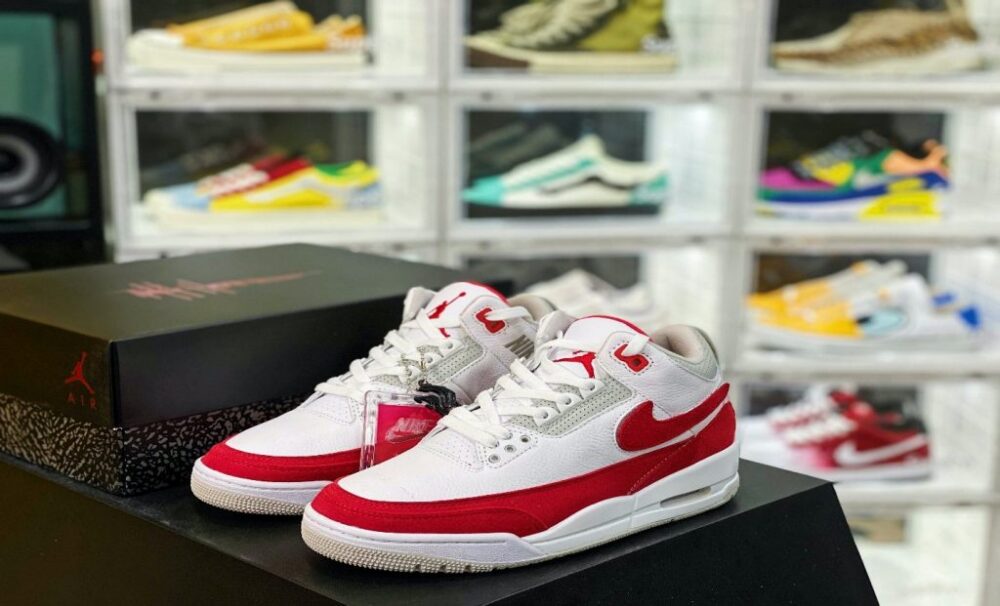 Red-and-white sneakers displayed on black shoe boxes in front of a wall of shoes