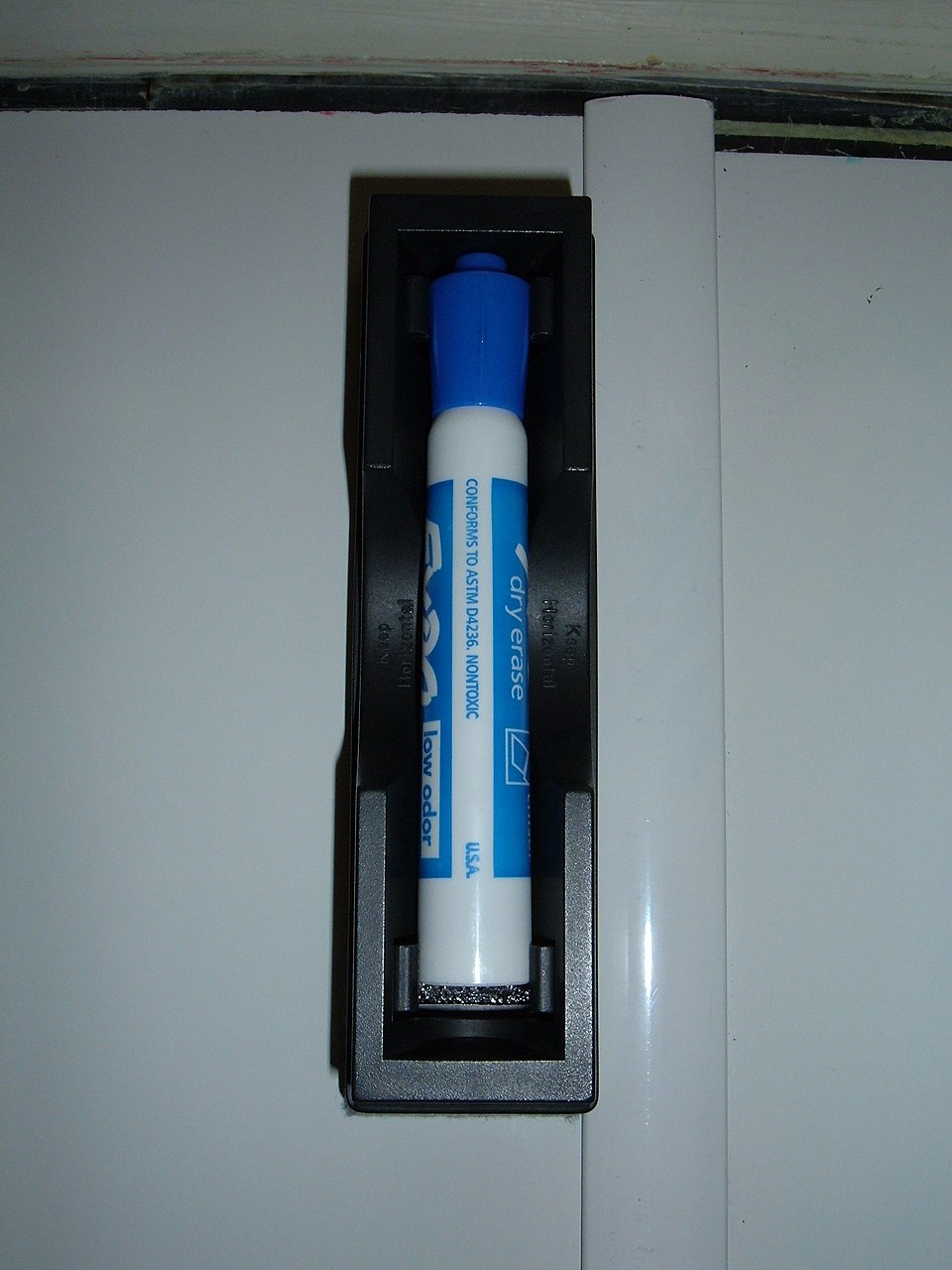 Blue dry-erase marker stored upright in a whiteboard-mounted holder.
