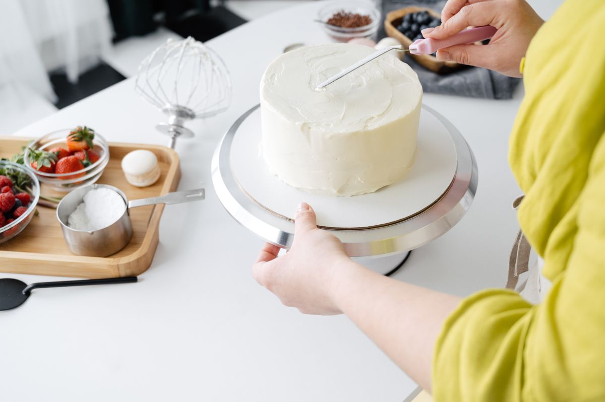 Baker smoothing cream on a cake placed on a rotating stand