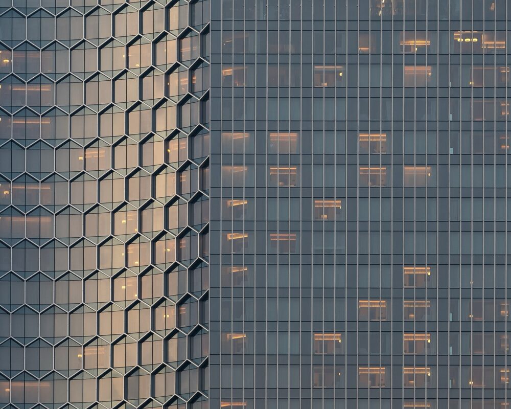 Exterior glass building with honeycomb pattern and warm interior lighting at sunset