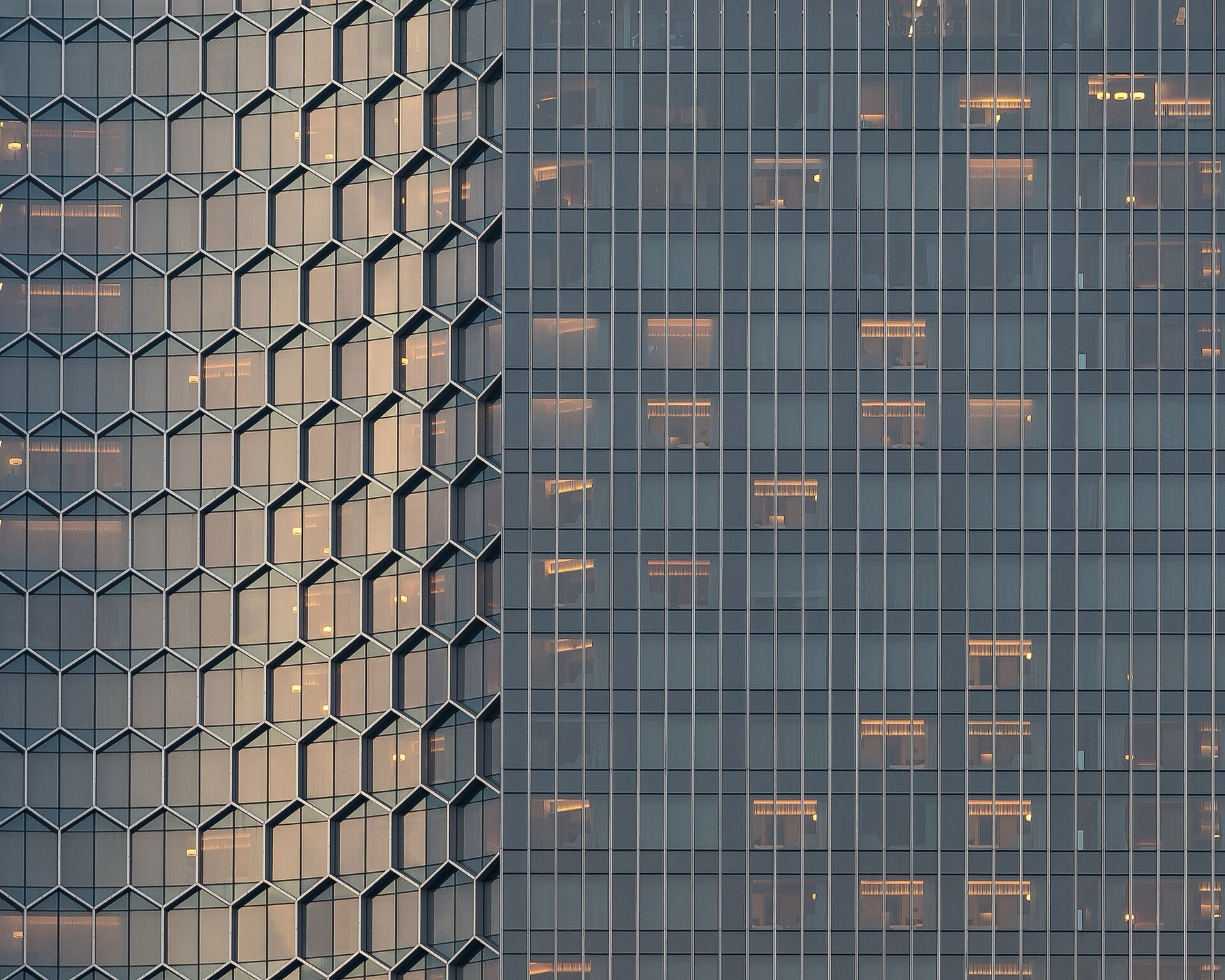 Exterior glass building with honeycomb pattern and warm interior lighting at sunset