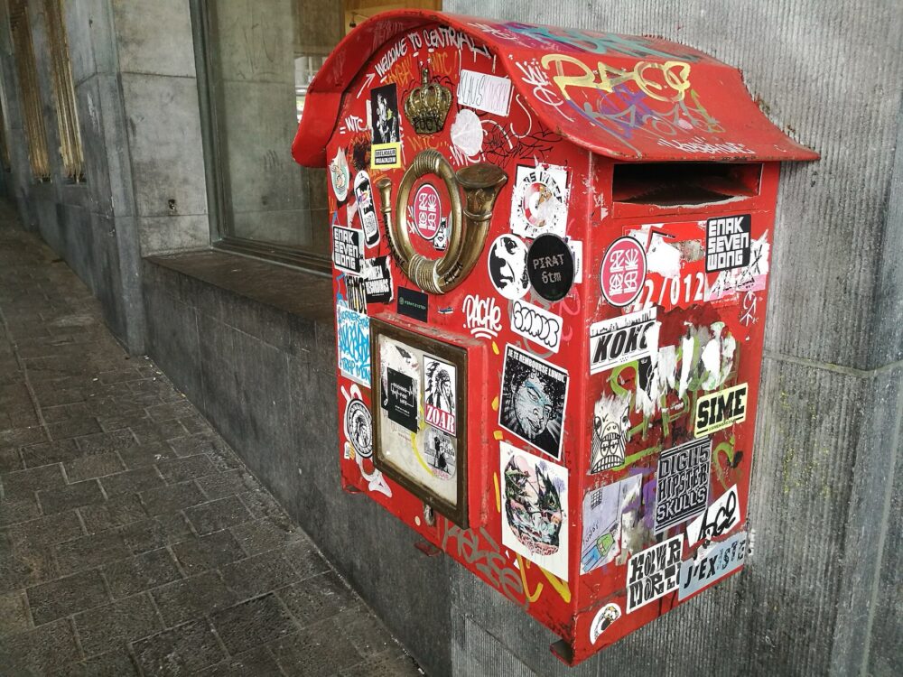 Assorted adhesive stickers on an urban mailbox, illustrating how different adhesives and backings behave on surfaces