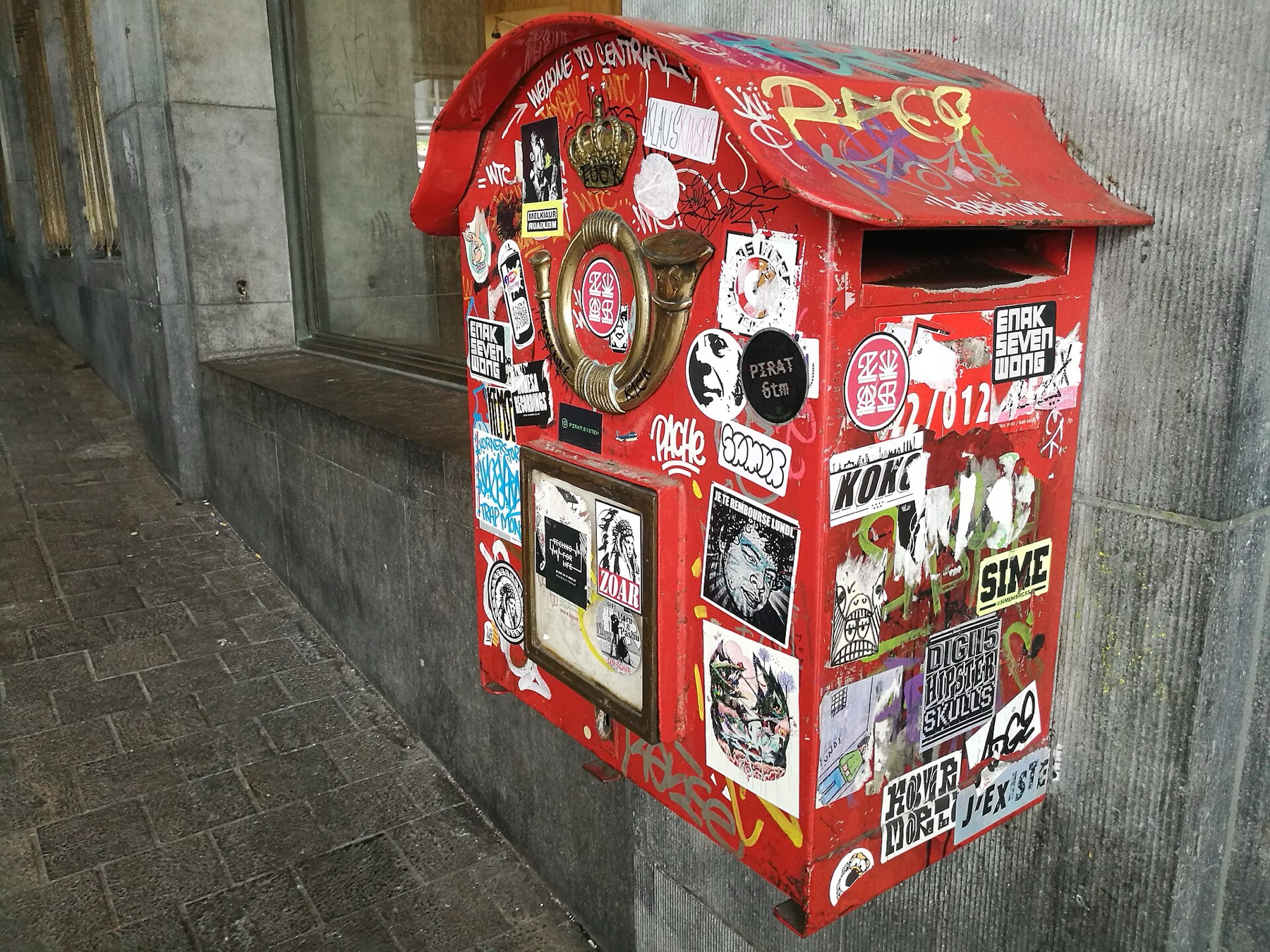Assorted adhesive stickers on an urban mailbox, illustrating how different adhesives and backings behave on surfaces