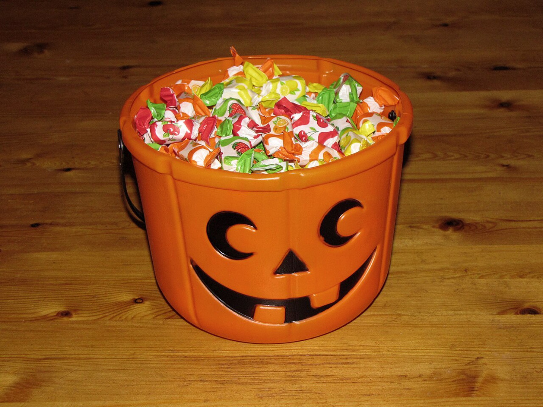 Orange plastic Halloween candy bucket full of wrapped treats on a wooden surface