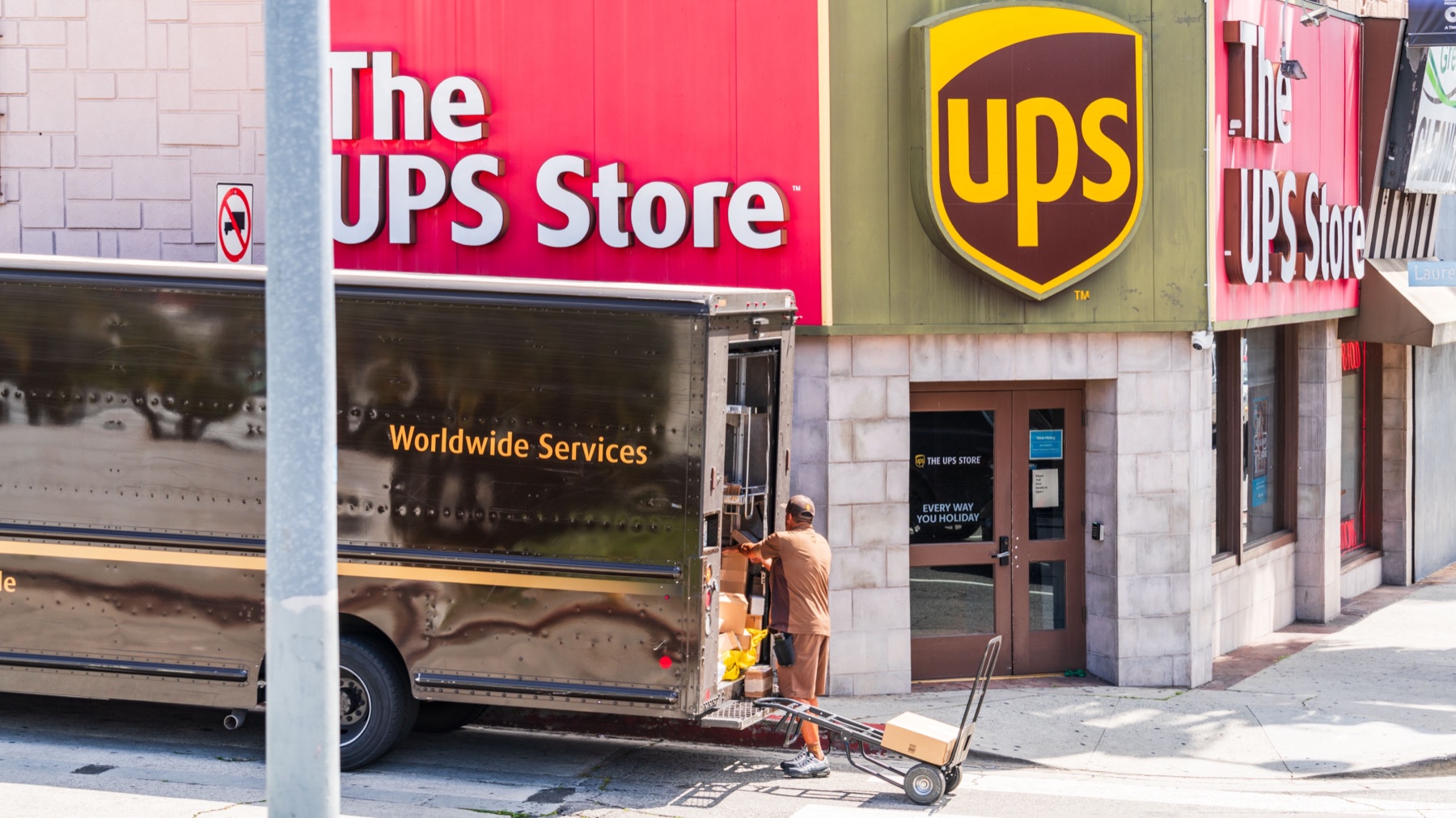 UPS driver delivering packages near a storefront, illustrating carrier-centric marketplace shipping workflows