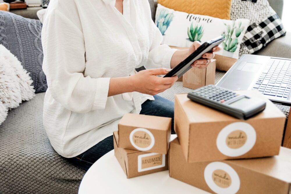 Online seller checking orders beside packing boxes, a laptop, and a calculator