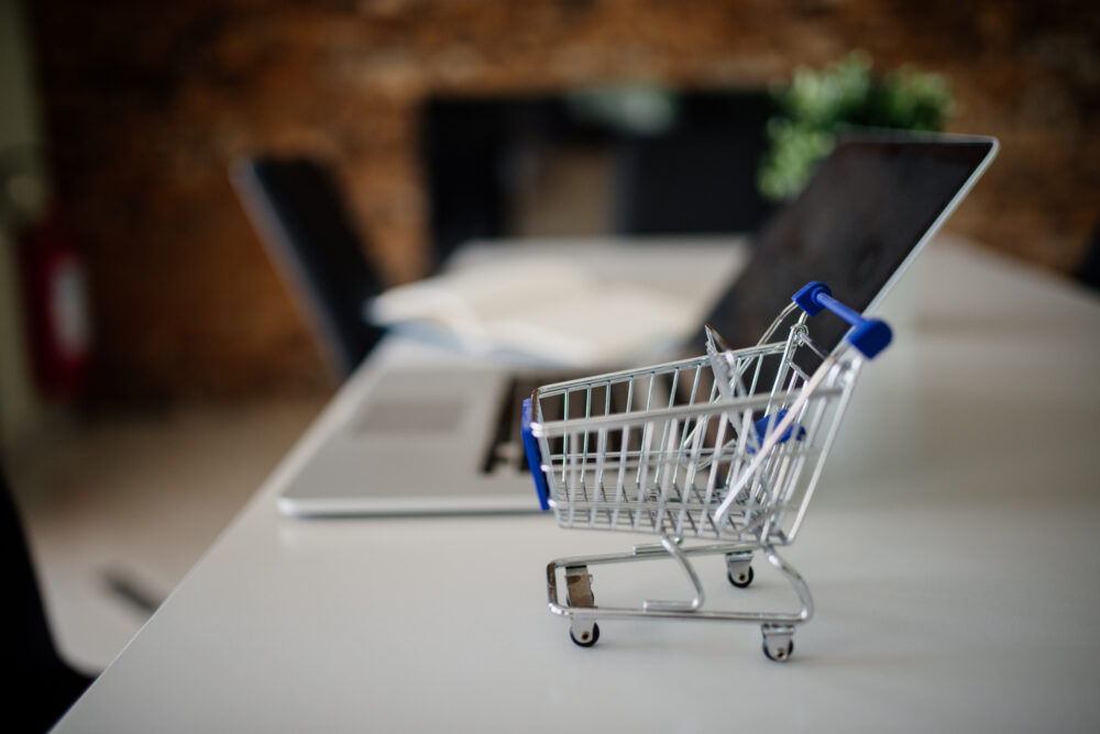 Miniature shopping cart beside a laptop, illustrating comparison of online shopping offers