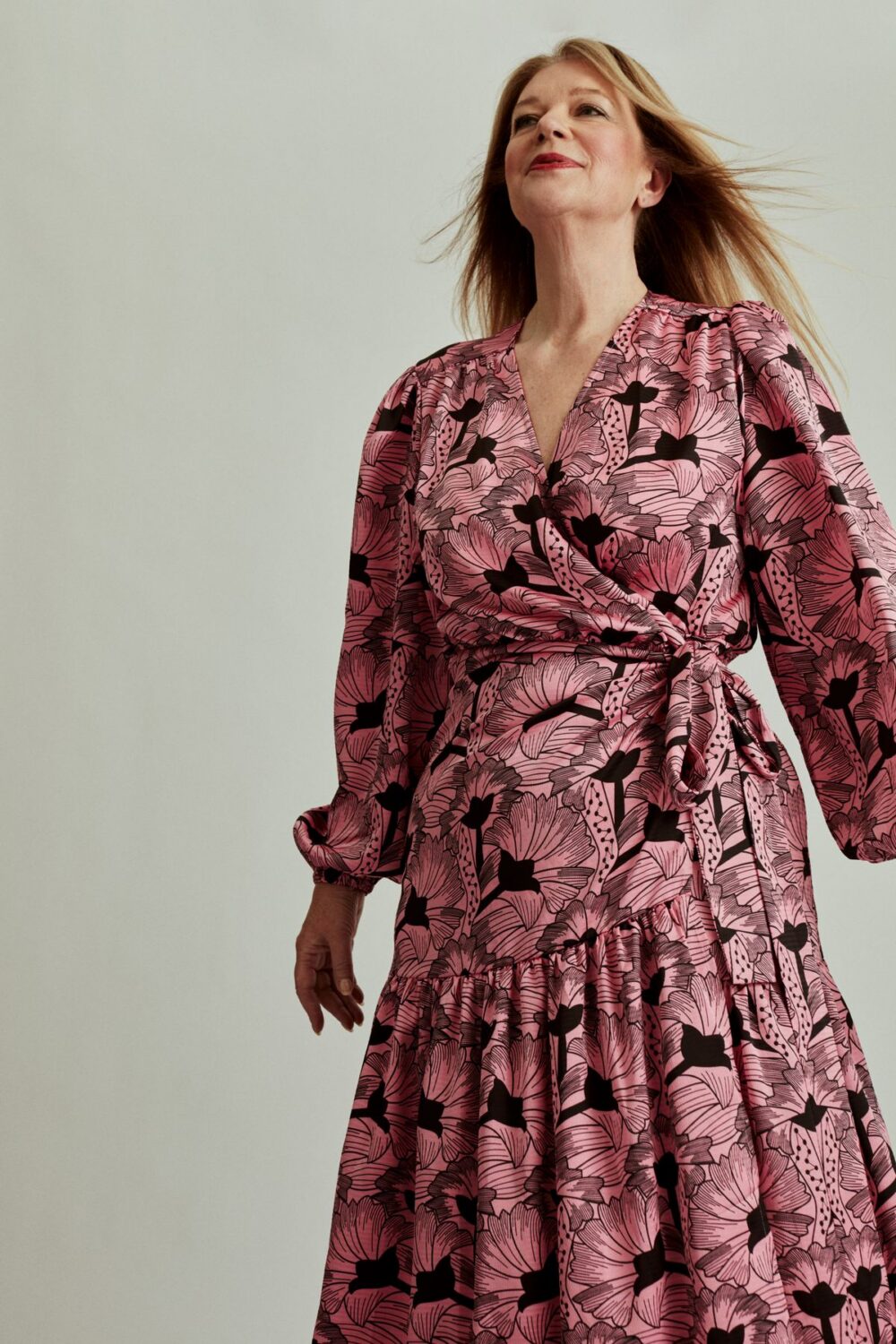 Woman wearing a pink floral dress with a crossover neckline and waist tie