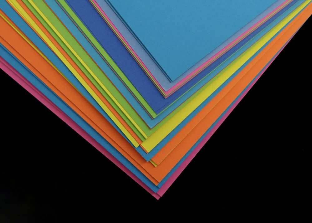 Stacked colored paper sheets showing the color and finish differences buyers should compare