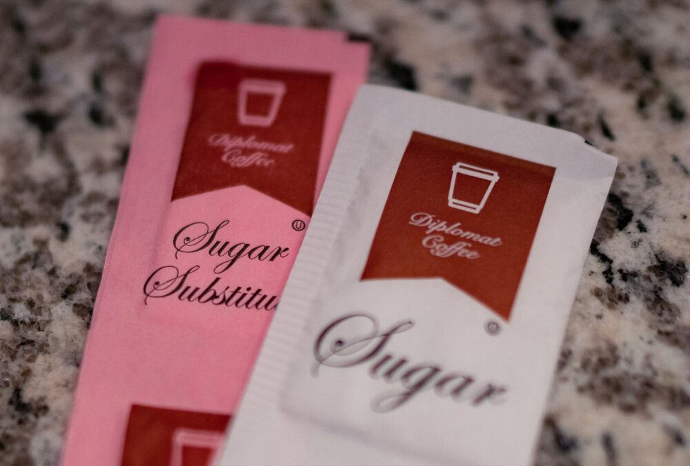 Bowl of sugar and packets of sugar substitute beside coffee cup
