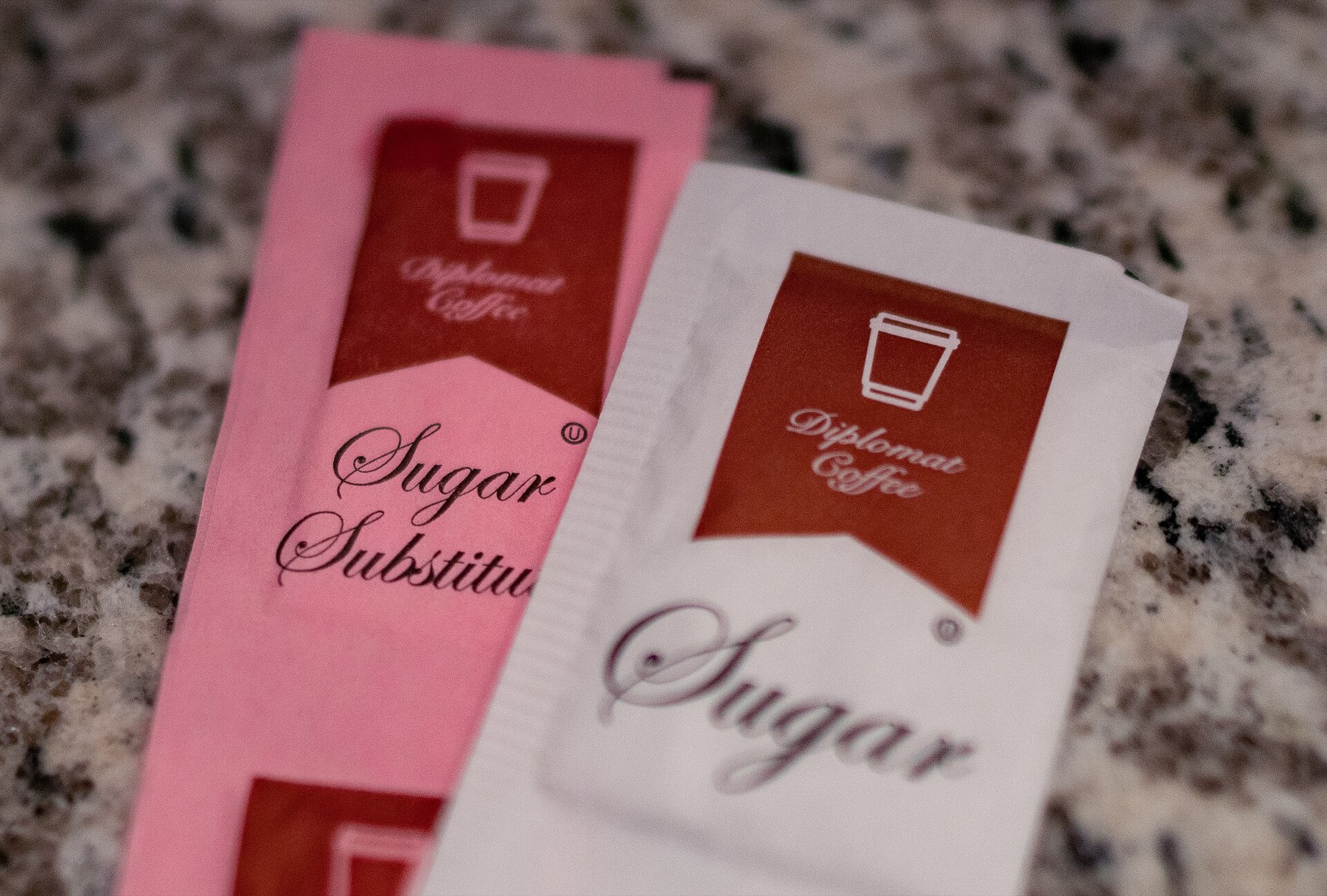 Bowl of sugar and packets of sugar substitute beside coffee cup