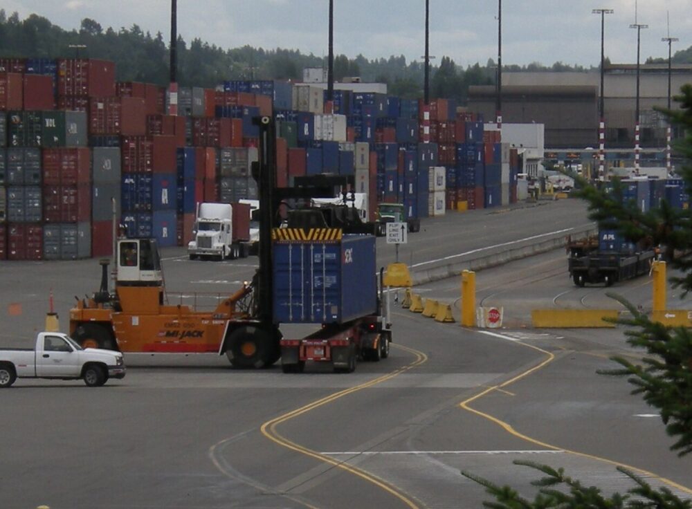 A shipping container being transferred between vehicles at a freight terminal, illustrating cross-border supplier logistics
