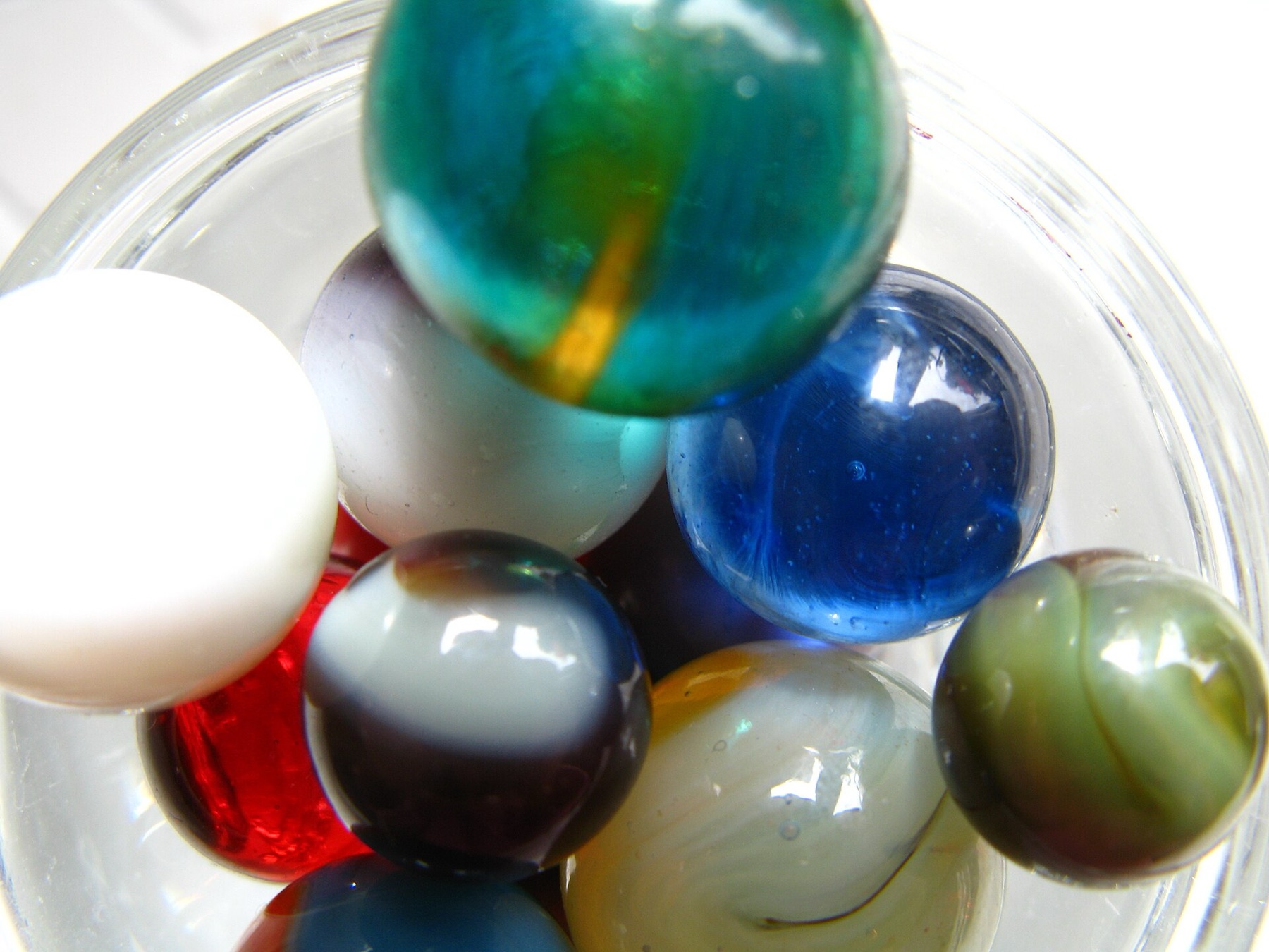 Assorted glass marbles in a clear container, showing variation in color and size