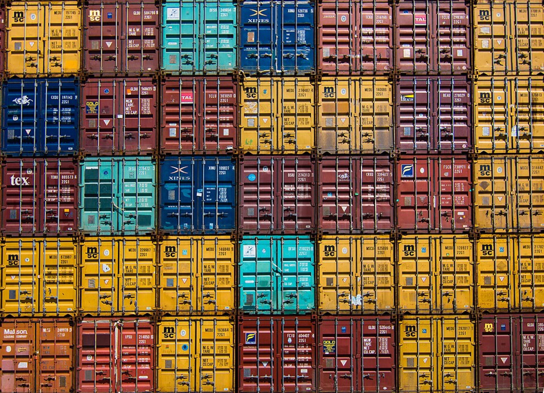 Pattern of multi-colored shipping containers stacked in rows, illustrating cross-border logistics complexity.