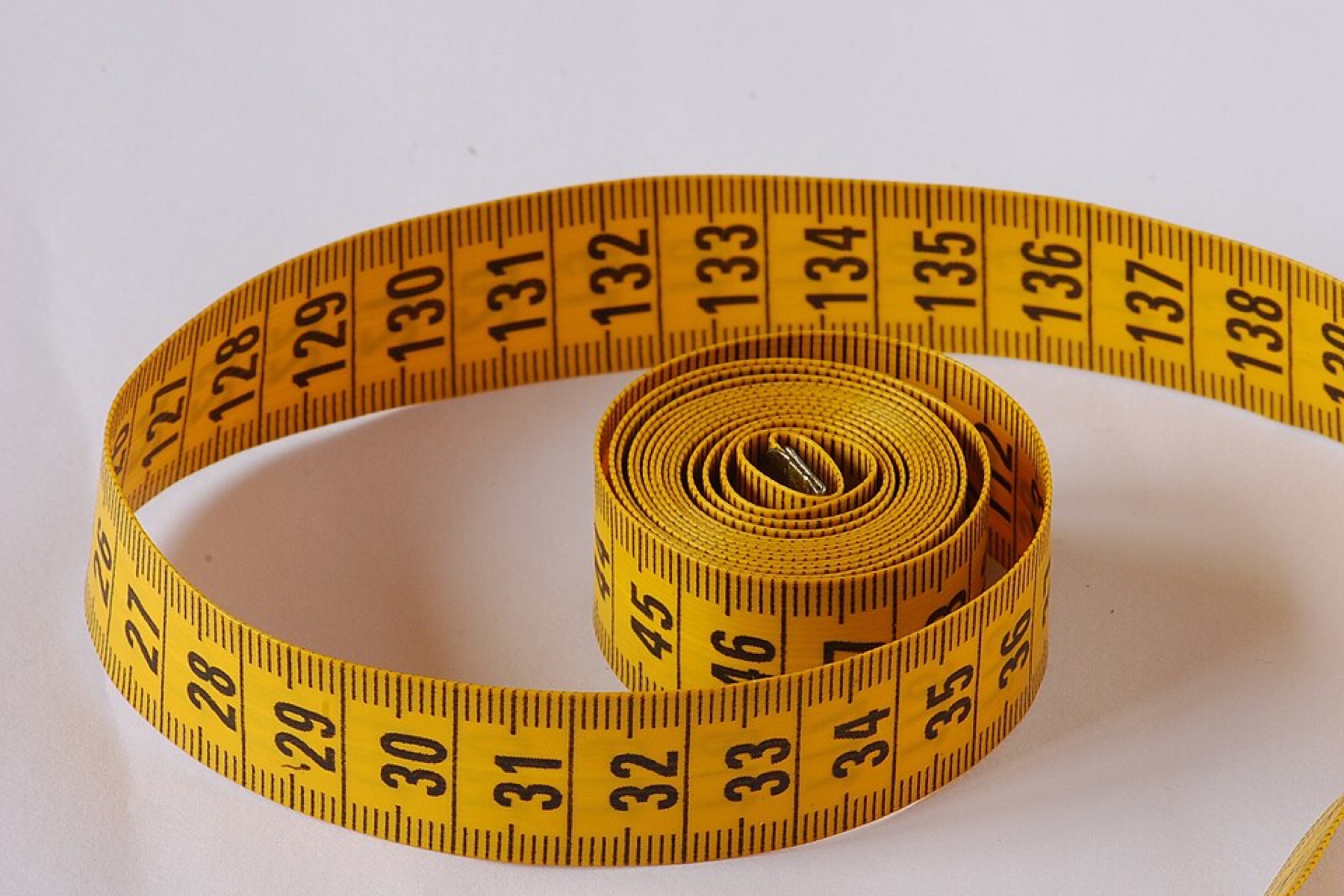Yellow flexible tape measure coiled on a white surface
