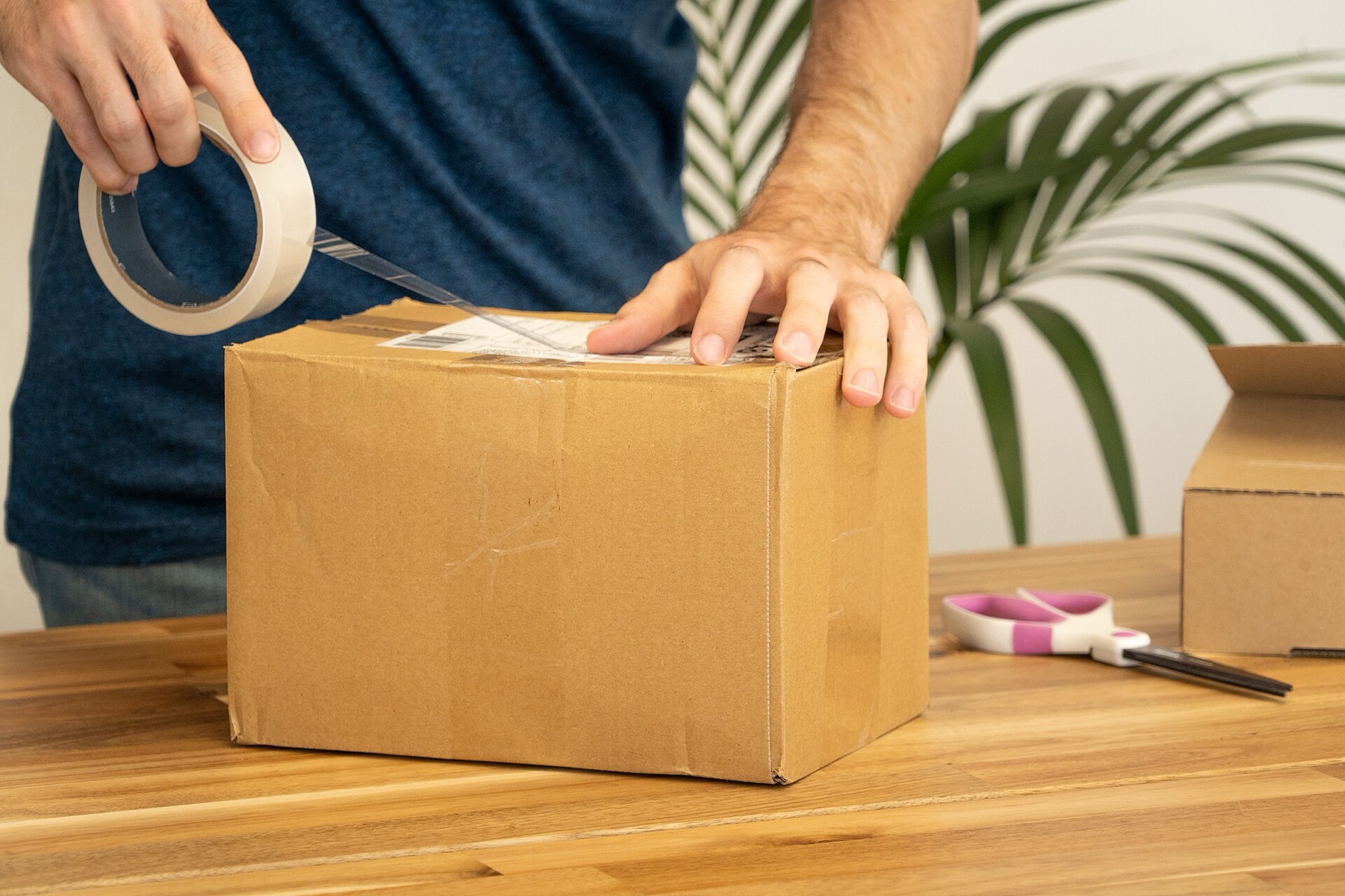 Person attaching a shipping label to a cardboard parcel, illustrating the importance of compliant packaging and labeling for resellers.