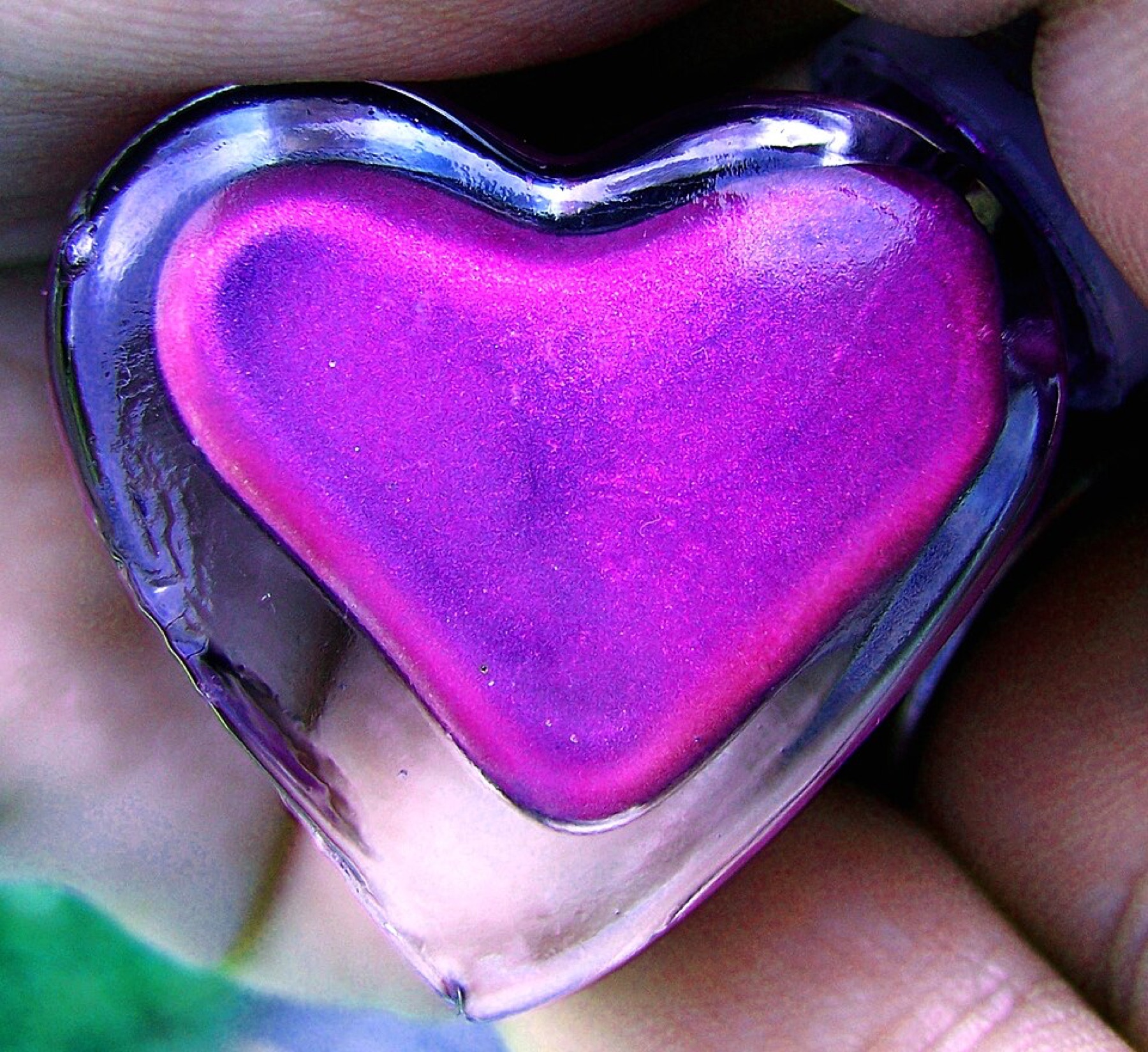 Heart-shaped pink and purple nail polish bottle on a reflective surface