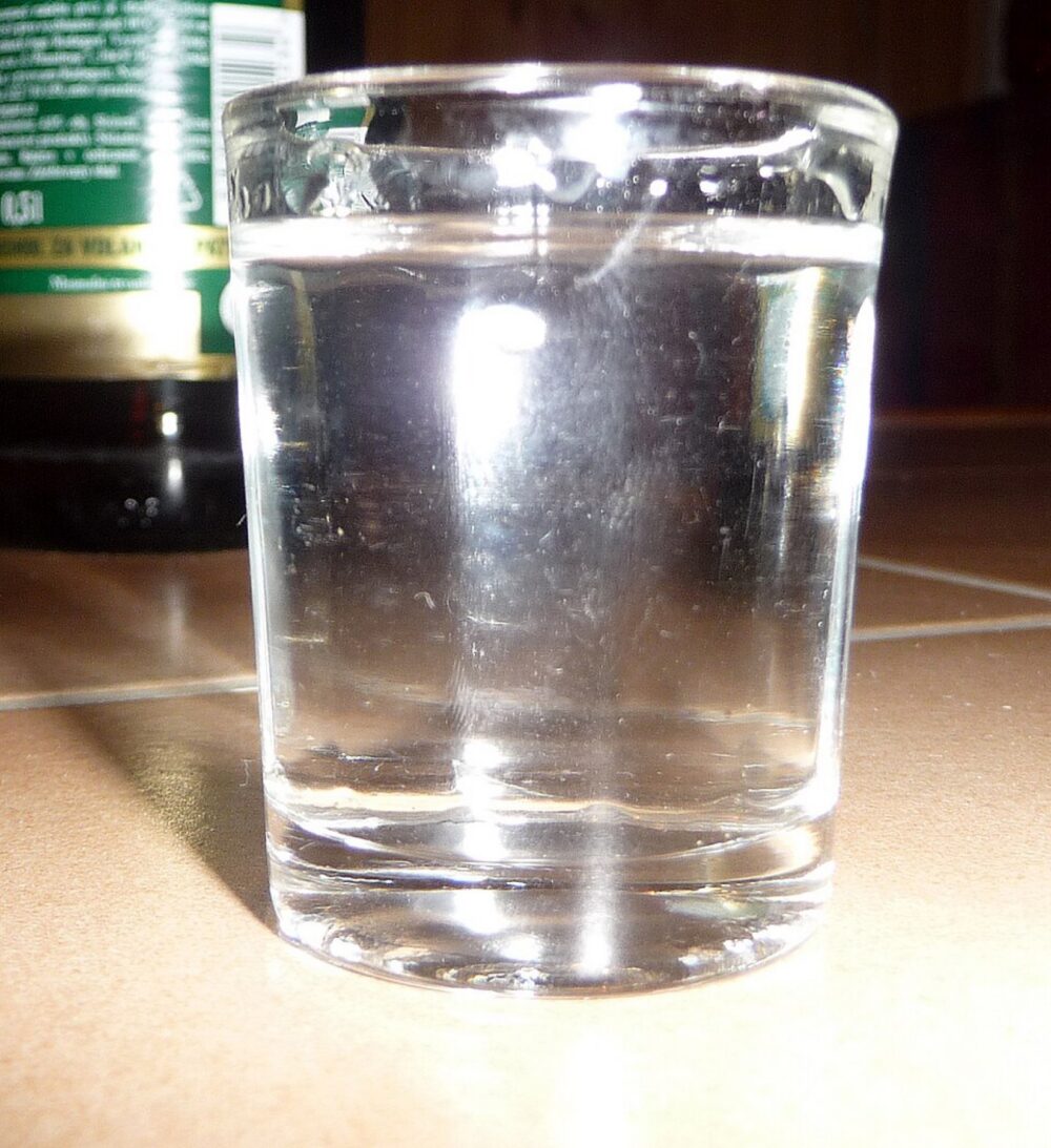 A clear glass shot glass filled with liquor, showing typical heavy base construction