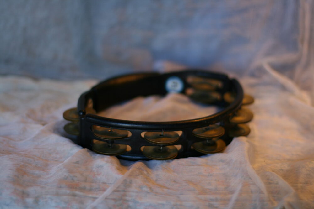 Black headless tambourine with paired metal jingles on a white cloth