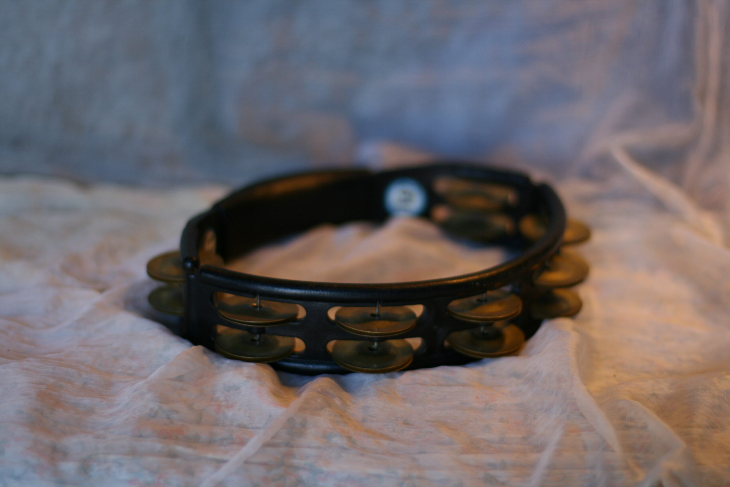 Black headless tambourine with paired metal jingles on a white cloth